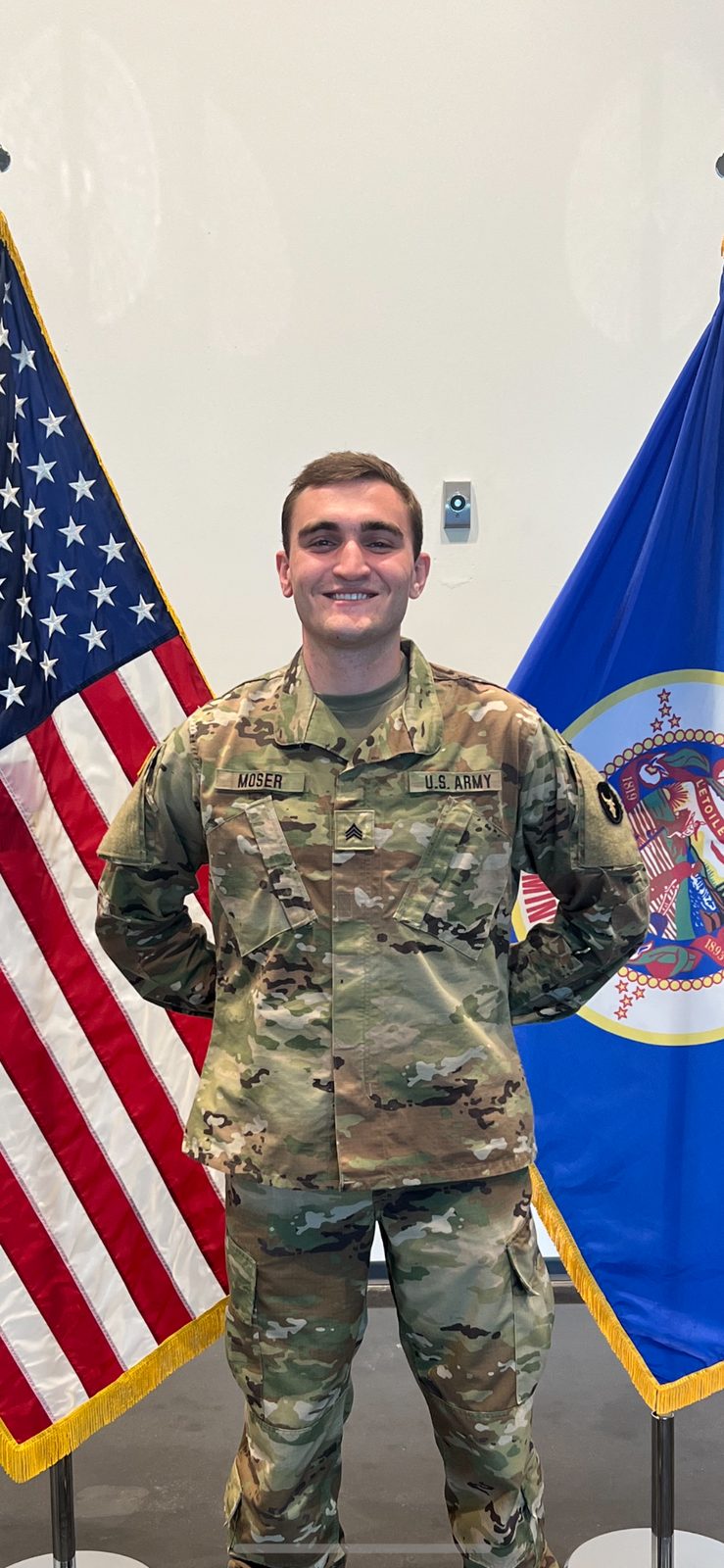 Dylan Moser in Army uniform standing between American and Minnesota flags.