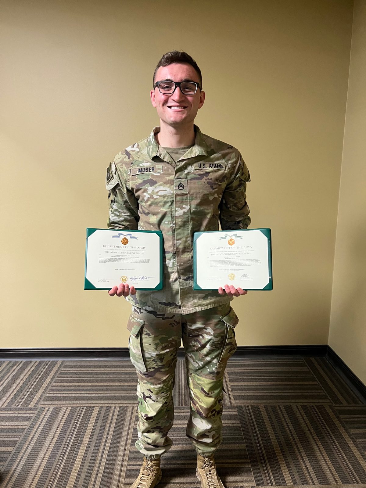 Dylan Moser in Army uniform holding Army award certificates.