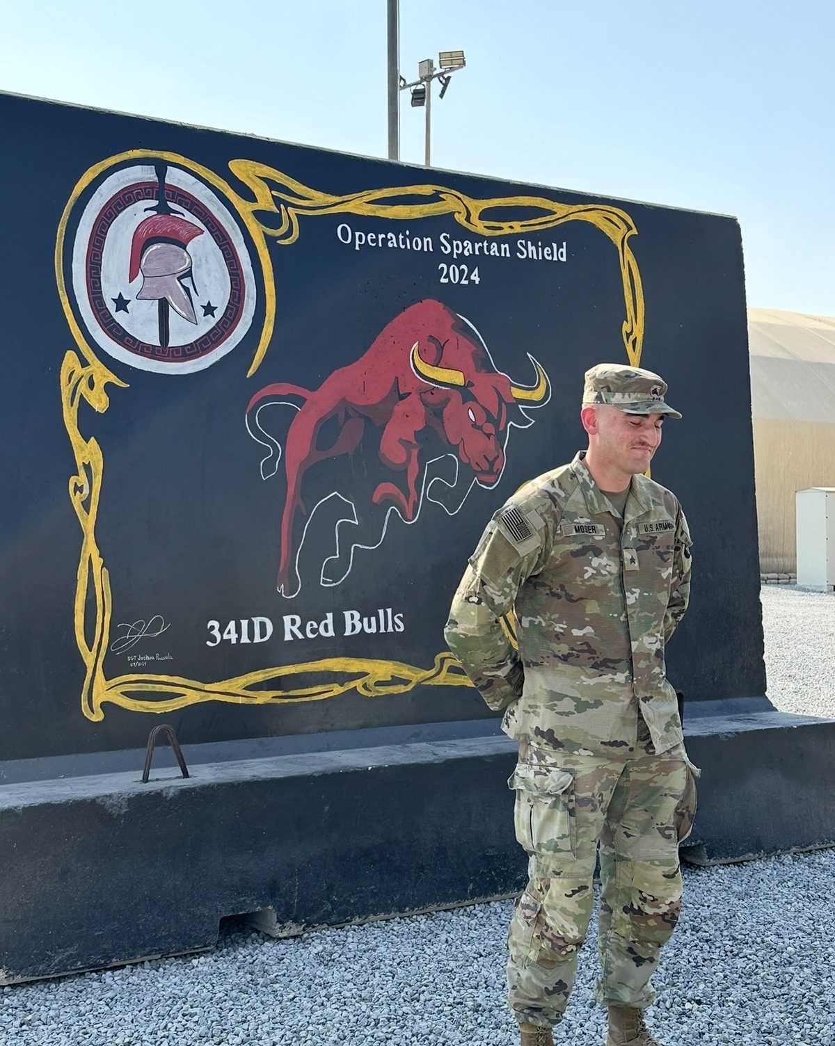Dylan Moser in Army uniform beside an Operation Spartan Shield 2024 34th Infantry Division Red Bulls display.