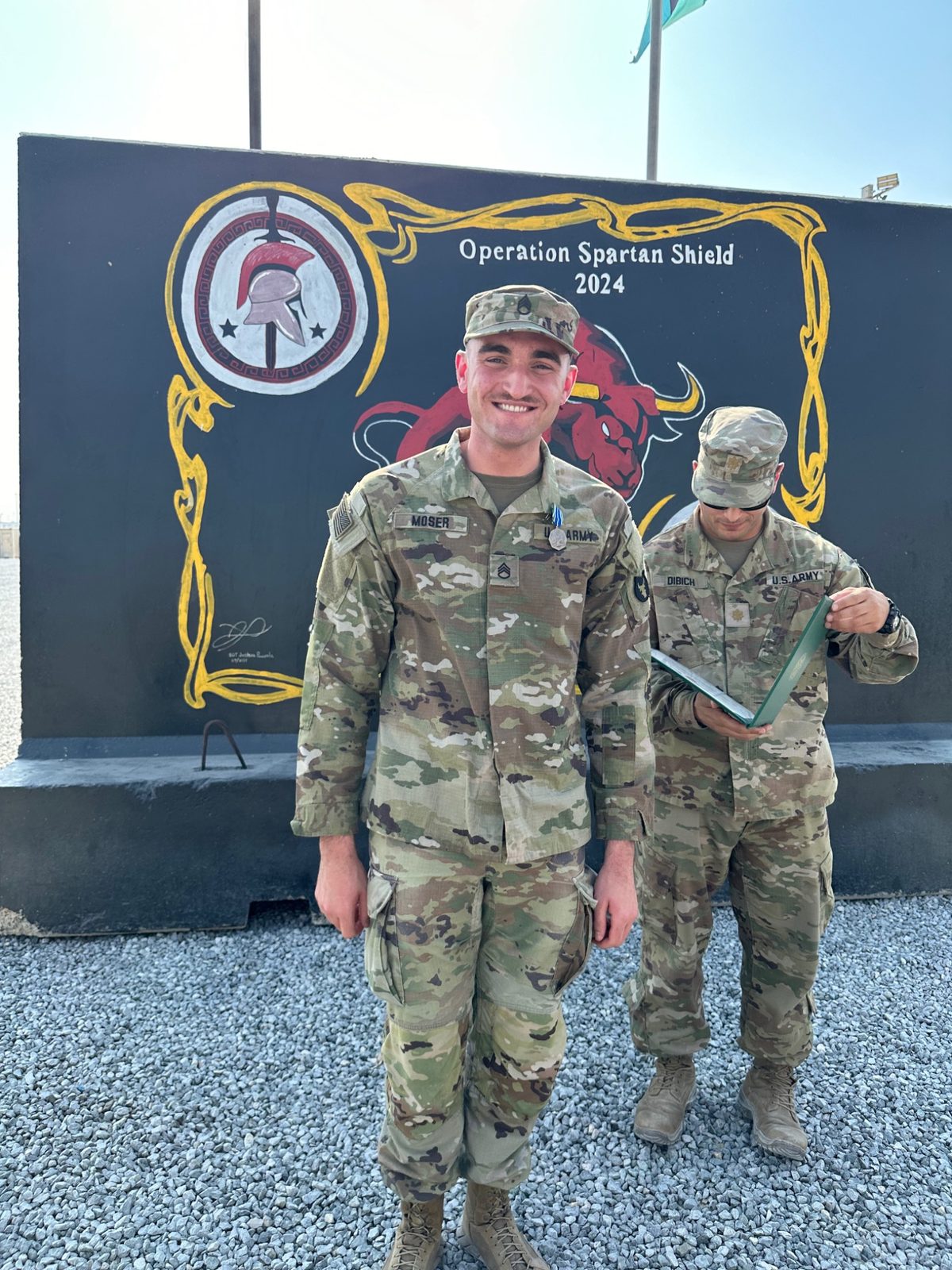 Dylan Moser smiling in Army uniform in front of a Red Bulls display during an award presentation.
